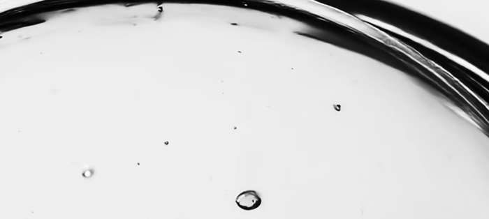 Primer plano macro de un líquido viscoso formando gotas y ondas, en blanco y negro
